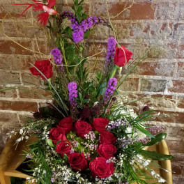 Tall arrangement of red roses and purple flowers in a wooden chair