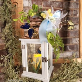 White lantern with butterflies, ribbon, and flowers on top