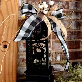 Black lantern with deer cutout topped by a plaid bow and white berries