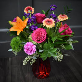 Mixed bouquet of roses, lilies, and gerbera daisies in a red glass vase