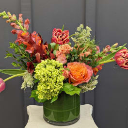 Mixed bouquet in a green glass vase with orange and pink flowers