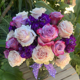 Bouquet of pink, white, and purple roses in a glass vase with a polka-dot ribbon