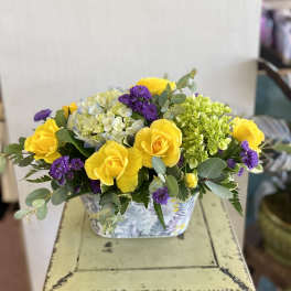 Yellow roses and purple flowers in a patterned rectangular container