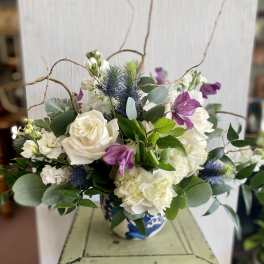 White roses and hydrangeas with purple blooms in a blue-and-white vase