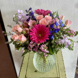 Mixed bouquet of pink, purple, and blue flowers in a textured glass vase