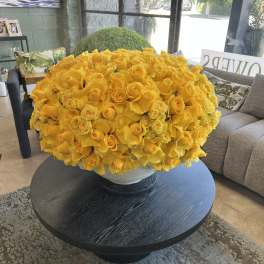 Large yellow rose arrangement in a white bowl vase on a round table