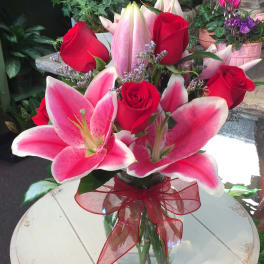 Bouquet of pink lilies and red roses in a glass vase with a red ribbon