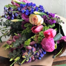 Mixed bouquet of pink peonies, roses, tulips, and purple and blue flowers wrapped in kraft paper