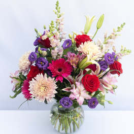 Mixed bouquet of red, purple, and pink flowers in a glass vase