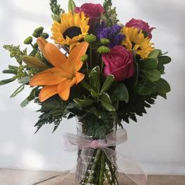 Mixed bouquet with sunflowers, roses, and an orange lily in a glass vase
