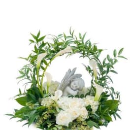 White roses and calla lilies arranged around a small angel figurine