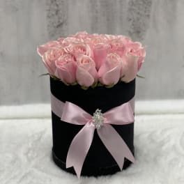 Round black hatbox filled with light pink roses and tied with a pink satin bow.