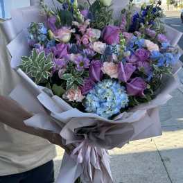 Large bouquet of purple, pink, and blue flowers wrapped in pale paper