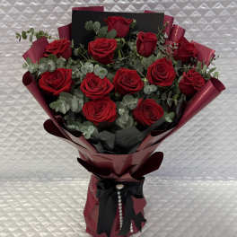 Bouquet of red roses wrapped in burgundy paper with a black ribbon