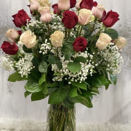Tall arrangement of red and pale pink roses with white baby's breath in a clear glass vase
