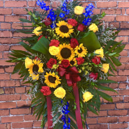 Standing floral spray with sunflowers, roses, and blue orchids on an easel