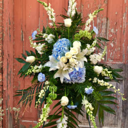 Tall floral spray with white lilies, blue hydrangeas, and white roses