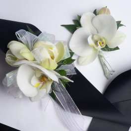 White orchid corsage and boutonniere with ribbon on black and white backing