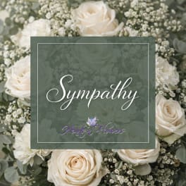 Cream roses and white filler flowers arranged around a sympathy card