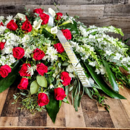 Large red and white casket spray with roses, lilies, and ribbon on a wooden surface