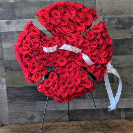 Standing spray of densely packed red roses in a cross-like shape on an easel with white ribbons.
