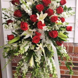 Tall standing spray of red roses, white lilies, and white flowers on a metal easel