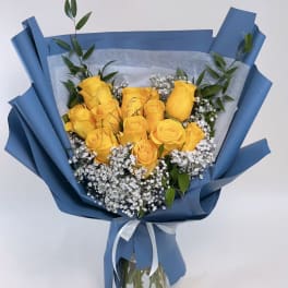 Yellow roses in blue wrapping with baby's breath in a glass vase