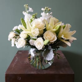 White lilies and roses arranged in a round glass vase