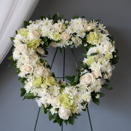 Heart-shaped floral wreath with white roses and chrysanthemums on a stand