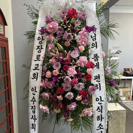 Tall standing floral wreath with pink and purple flowers and white ribbons