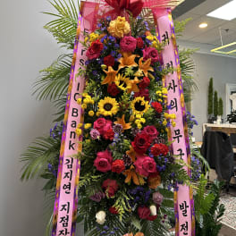 Tall standing floral wreath with pink ribbons and mixed blooms