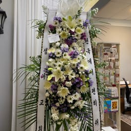 Tall standing floral wreath with white and purple flowers and ribbon streamers