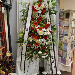Tall standing floral spray with white ribbons and red, white, and orange flowers