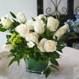 White roses arranged in a square glass vase with green foliage