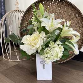 White lilies and pale flowers in a white vase with a cross emblem