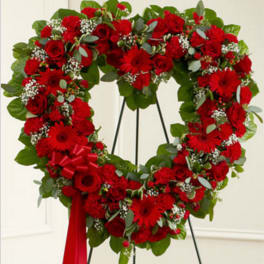 Heart-shaped wreath of red flowers with a red ribbon on a stand