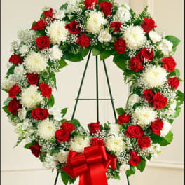 Heart-shaped wreath of red and white flowers on a stand with a red bow
