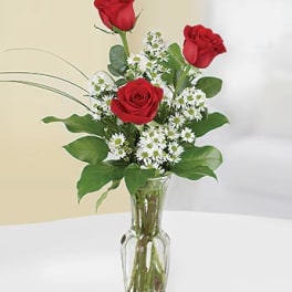 Tall arrangement of three red roses with small white daisies in a clear glass vase