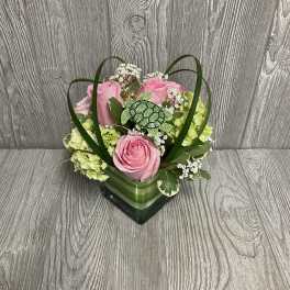 Pink roses and green hydrangeas in a square glass vase with a turtle pick