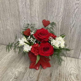 Red roses and white flowers in a red boot-shaped vase with glitter hearts