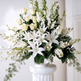 White lilies and pale roses in a white pedestal vase
