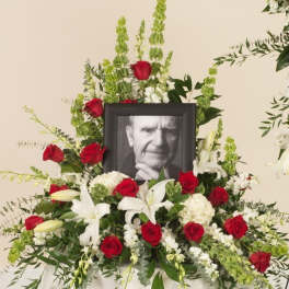 Sympathy floral display with red roses, white lilies, and a framed portrait