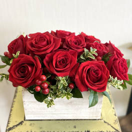 Red roses arranged in a white wooden box with berries and greenery