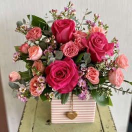 Pink and coral rose bouquet in a striped gift box with a heart charm