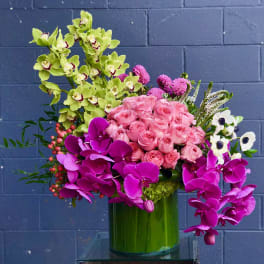 Pink roses and orchids arranged in a green glass vase