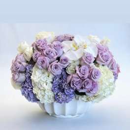 Lavender roses and white orchids arranged in a white vase