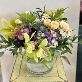 Mixed bouquet in a glass vase with orchids, roses, and purple blooms