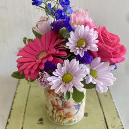Mixed pink and purple flowers in a floral tin vase