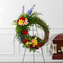 Colorful floral wreath on a stand beside a casket
