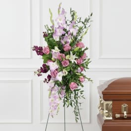 Tall floral spray with pink roses and lavender lilies beside a casket